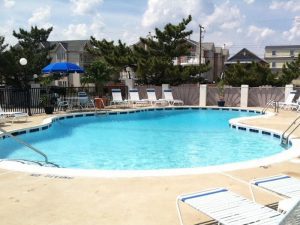 A full shot of a pool filled with water and benches with unbrella on the pool side.