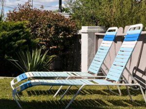 A close-up of pool chairs on green grass against the sunlight.